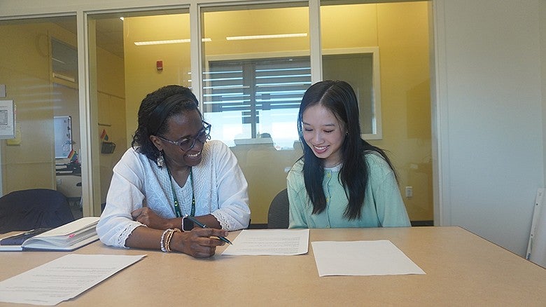 two individuals sitting at a table talking while looking down at paperwork