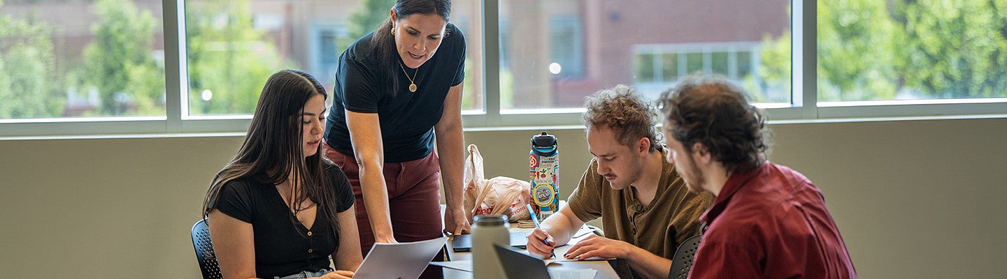 students sitting at a table while a professor is teaching them