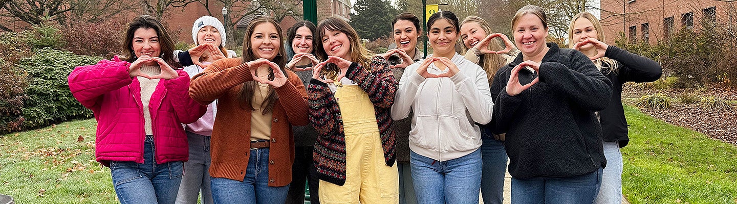 group of students forming an O with their hands while standing in front of the HEDCO building