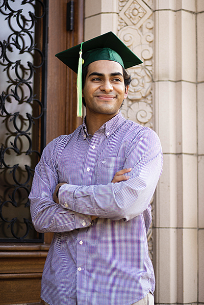 Gilberto Orozco standing against a wall with arms crossed wearing grad cap