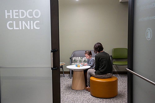 Individual sitting with a child at a table playing with toys inside the HEDCO Clinic