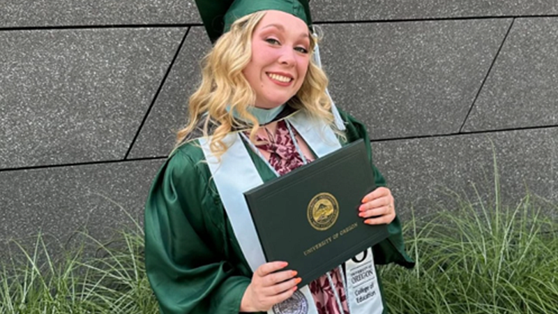 Emily Westlund in graduation regalia holding her College of Education degree