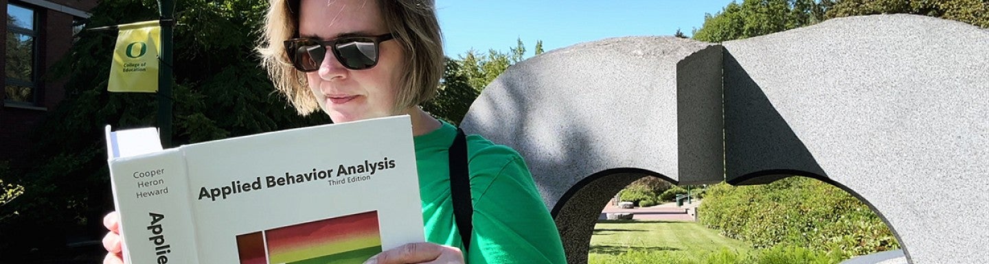 student holding an ABA textbook while sitting by the HEDCO building outside artwork
