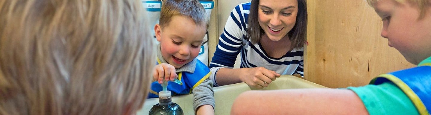 A person working with young students at a sink