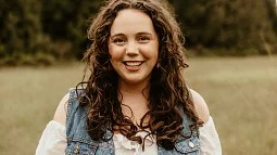 alumni Lily Smith standing in a field with trees in the background