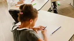 young individual in a classroom setting sitting at a desk writing