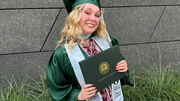 Emily Westlund in graduation regalia holding her College of Education degree