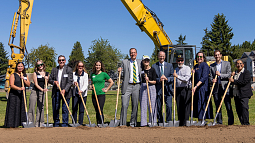 group of individuals standing in a line holding shovels in dirt for a ground breaking ceremony