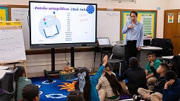 teacher in a classroom standing by a screen