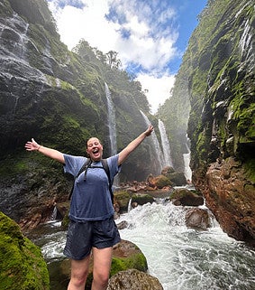 Ellie Hein with arms raised standing in front of a waterfall in Costa Rica