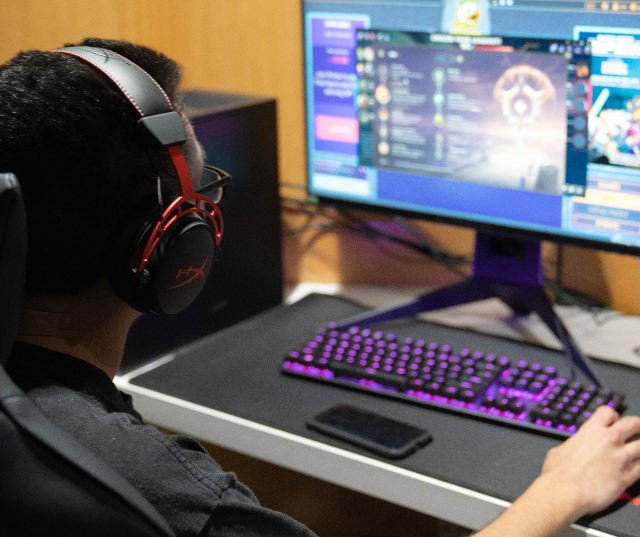 Student gaming with illuminated keyboard inside Esports Lounge.