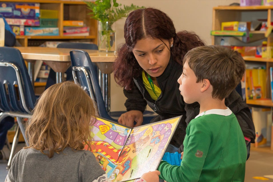 Moss staff showing book to two children.