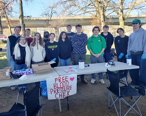 A group of young adults stand in a park offering free blood pressure checks