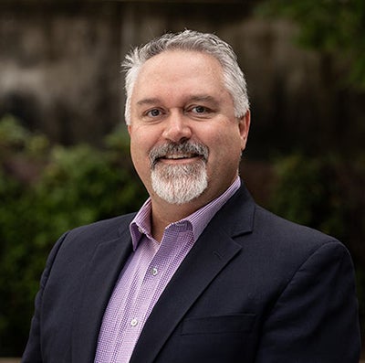 Man with graying hair and a beard wearing a dark blue suit