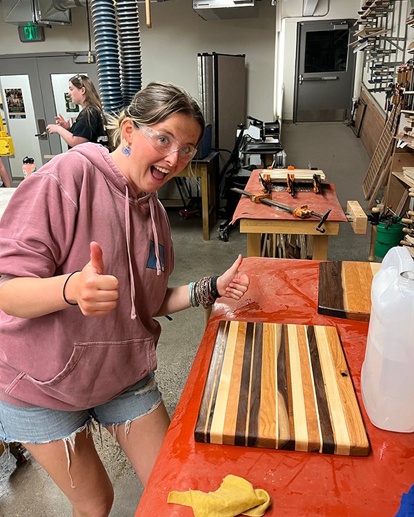 Young woman holds two thumbs up after crafting a wooden cutting board