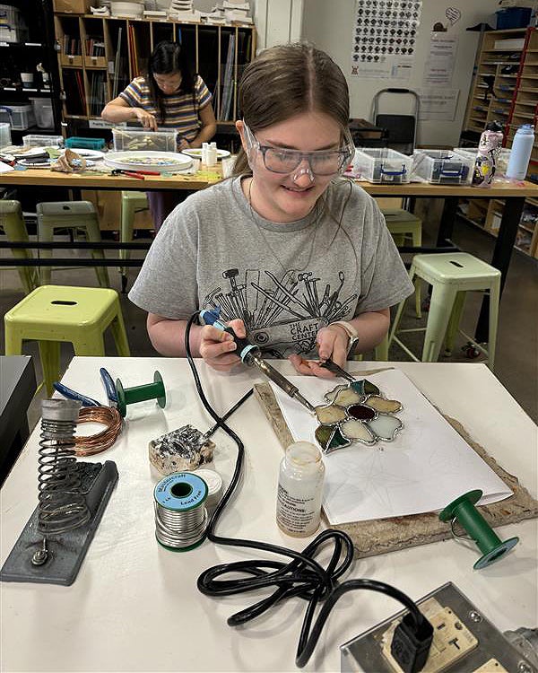 Young woman melts metal to solder a stained glass flower