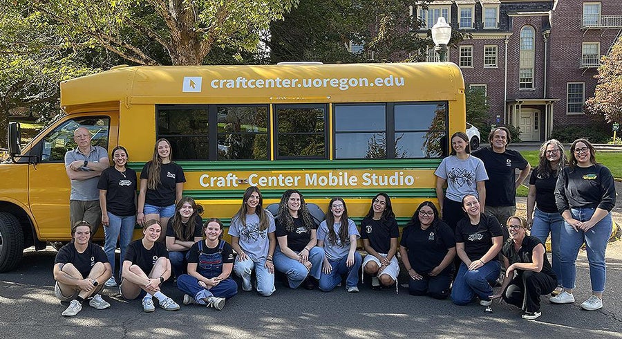 Multiple people stand, kneel, and sit in front of a yellow bus