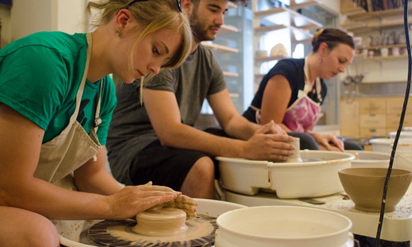 Students working on clay pottery with clay wheel spinner.