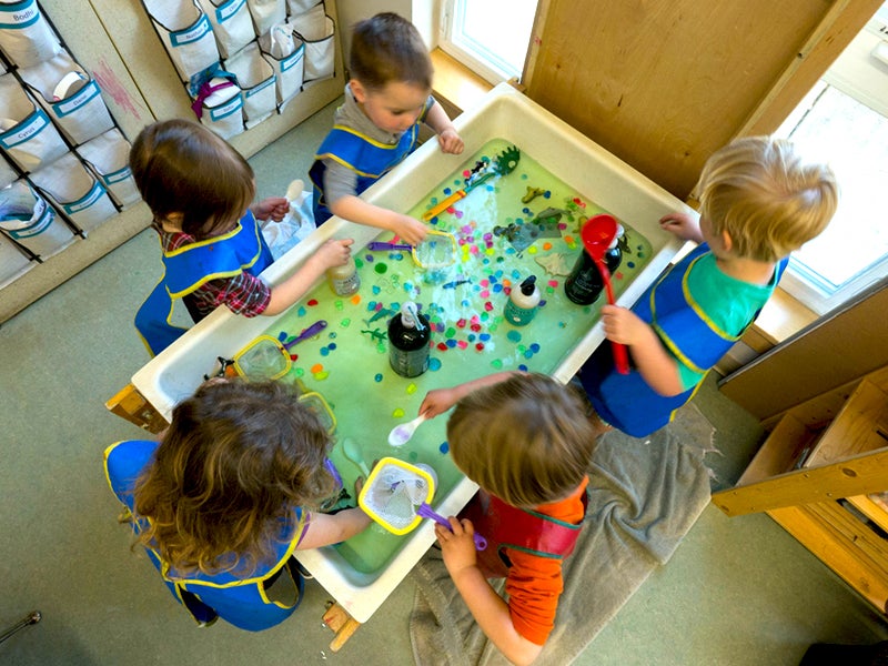 Children at water table scooping water, and play with water toys.