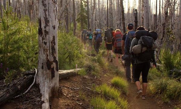 Students hiking on hiking path with camping backpacks and gear.