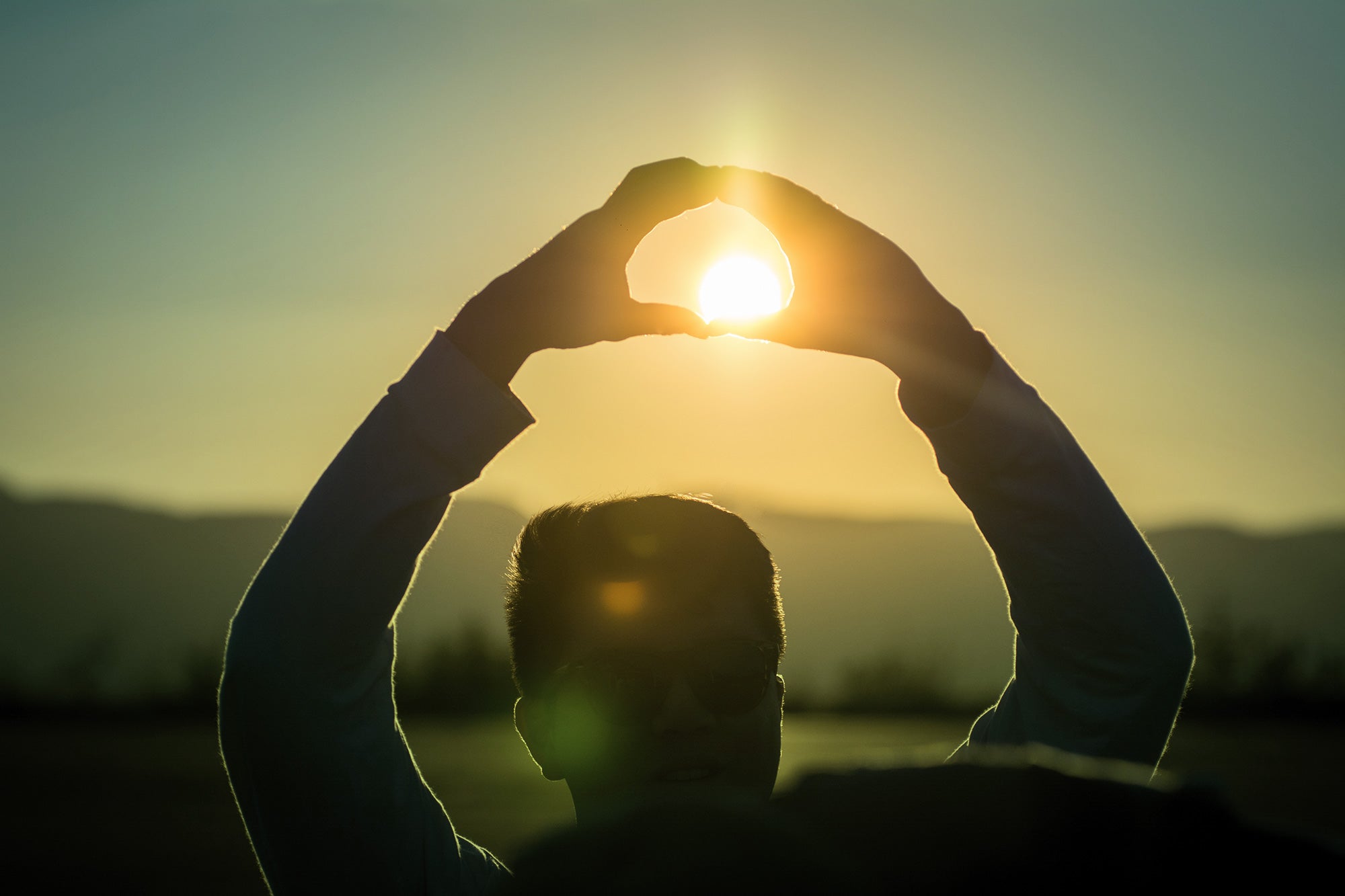 Student lifting hands in a UO "O" shape around the setting sun