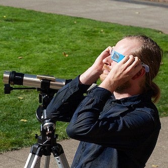 jesse feddersen with telescope on UO green, looking at the sky with eclipse glasses on