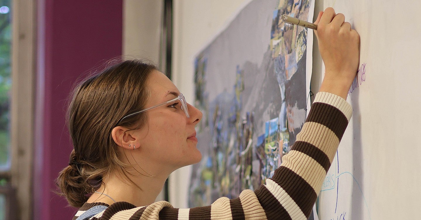 student mia owen writing on paper on the wall with a graphic chart on it and an abstract poster in the background