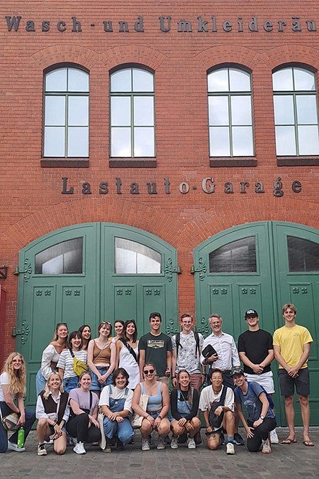 group of students posing outside brick building with german words on it