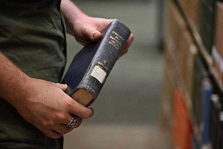 hands holding a book with gold lettering on spine in a library stack