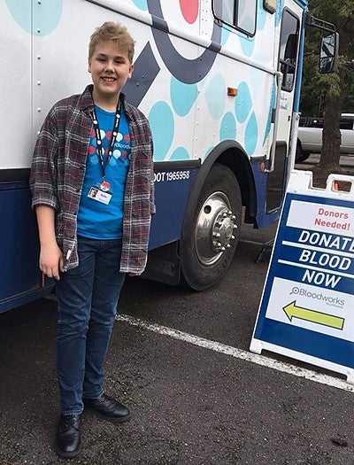 teenage boy posing next to blood donation vehicle