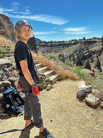 teenager looking over ravine wearing rock climbing gear, smiling on sunny day