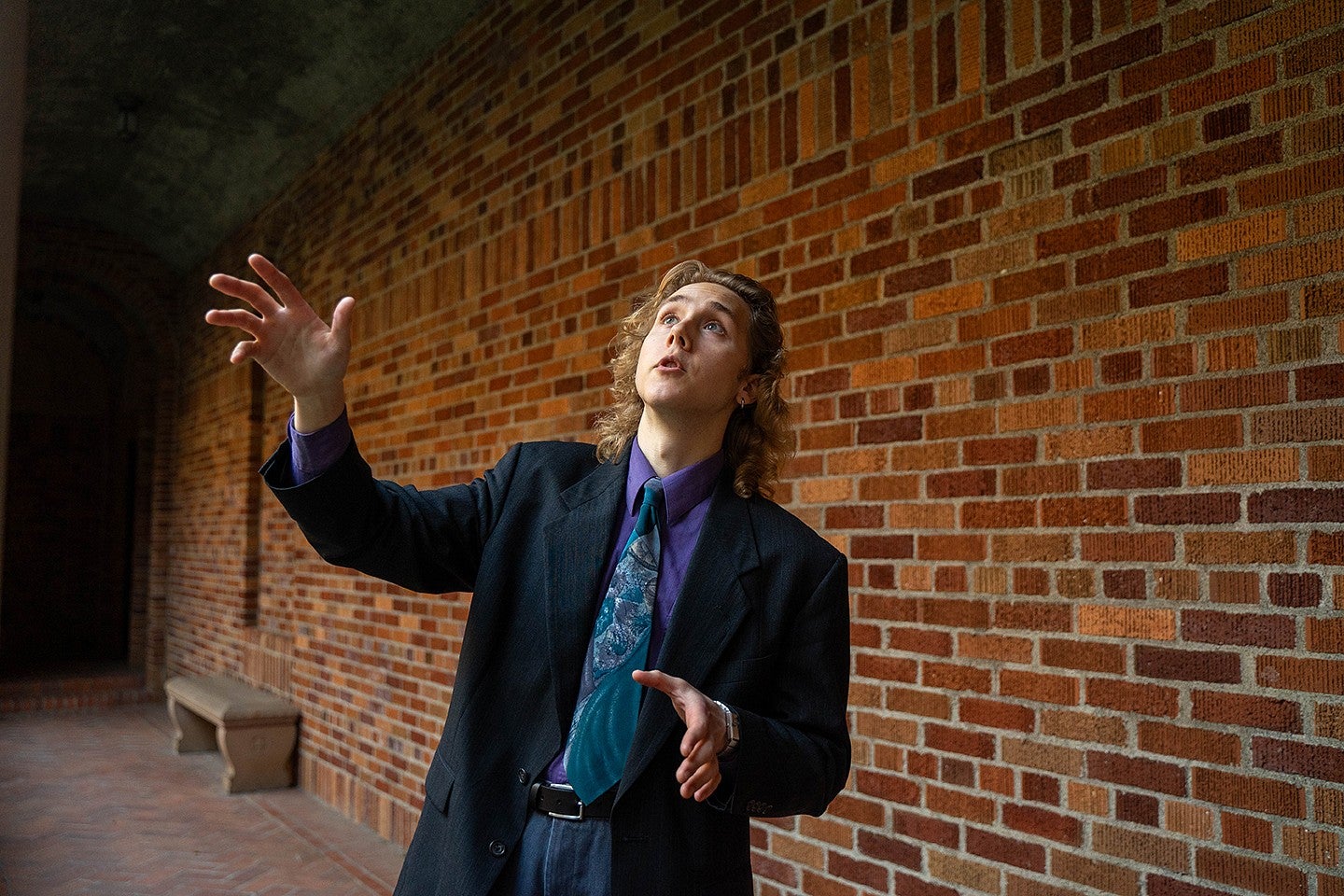 dylan podrabsky wearing a suit and gesturing in front of a brick wall