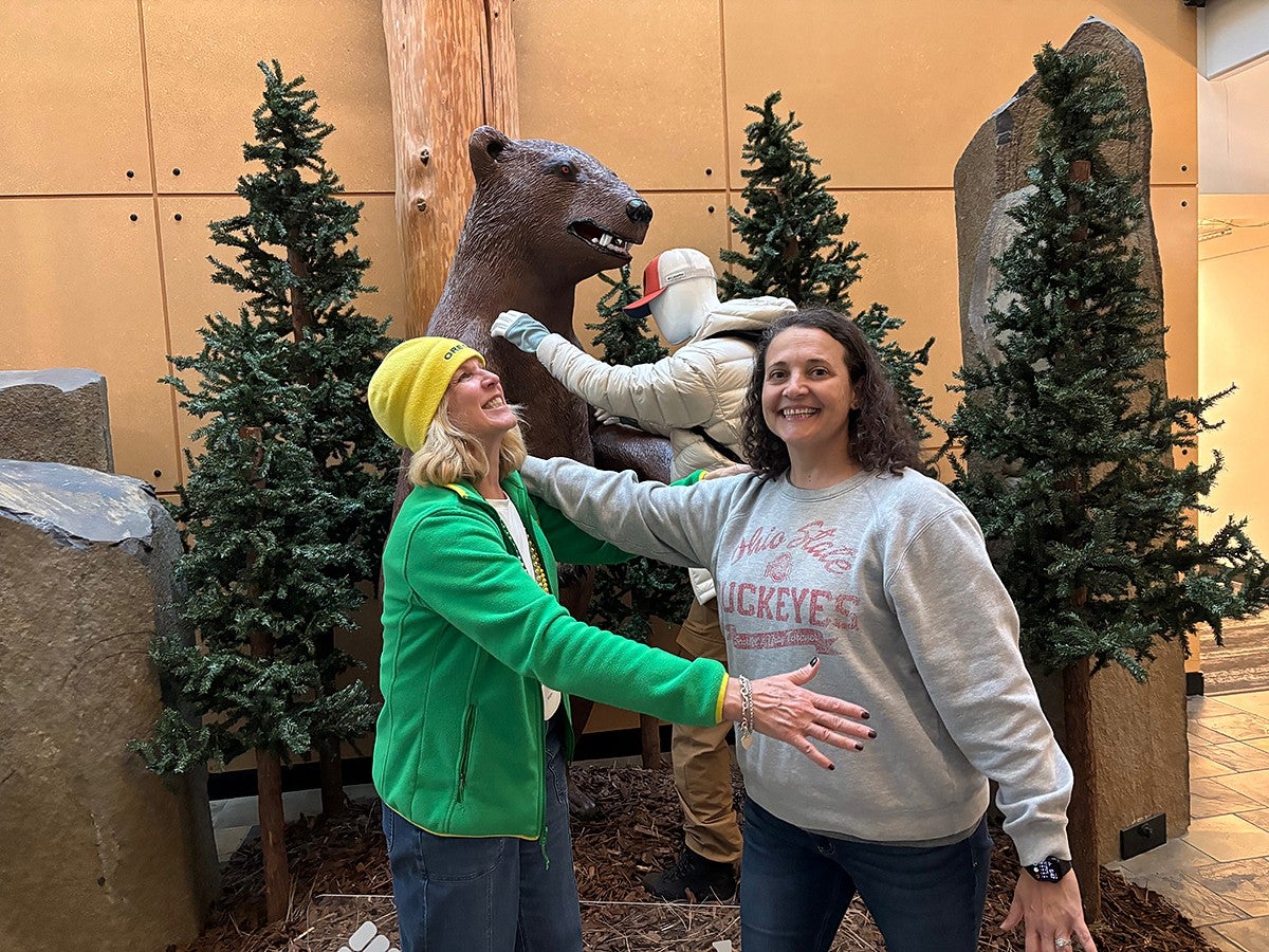 two people mimicking a mannequin fighting a bear statue behind them