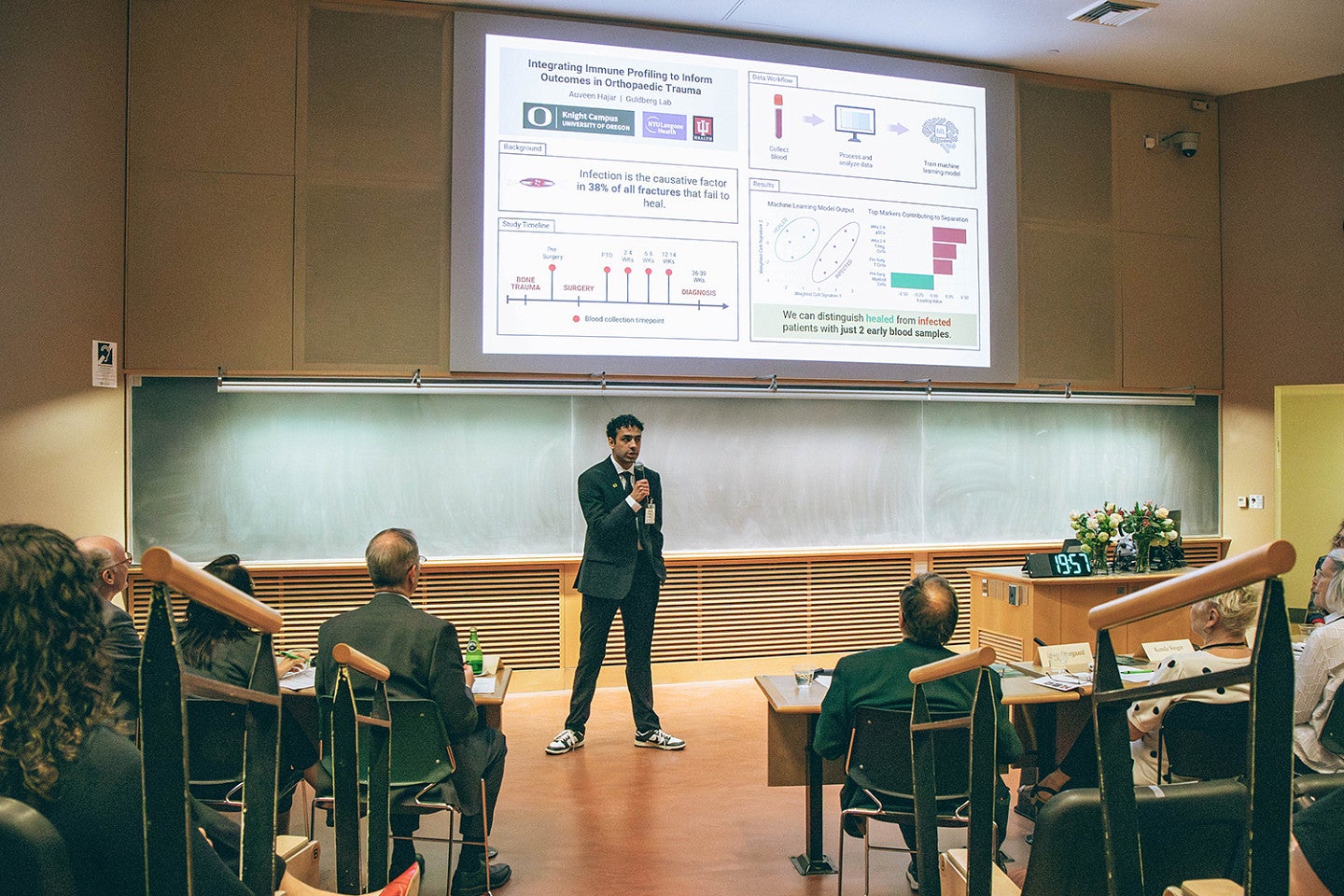 auveen hajar presenting to auditorium at three minute thesis 2026 under digital slide
