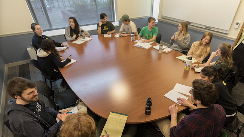 students seated around large classroom table, engaged in partner work