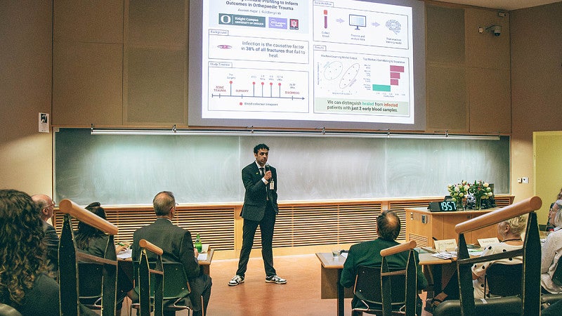 auveen hajar presenting to auditorium at three minute thesis 2026 under digital slide
