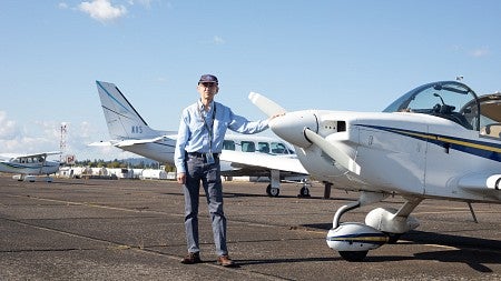 robert mauro posing next to small plane on runway, wearing NASA cap