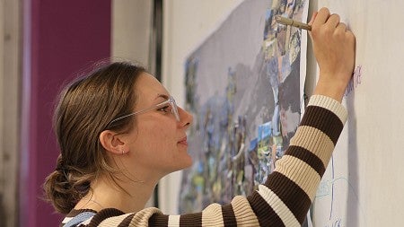student mia owen writing on paper on the wall with a graphic chart on it and an abstract poster in the background