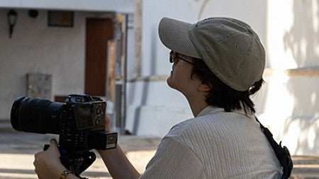 person crouching in courtyard with video camera on monopod, looking up at buildings