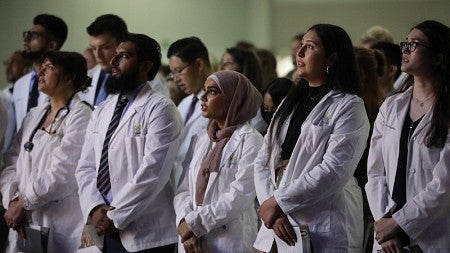 medical students in white coats standing at an initiation ceremony, reciting an oath