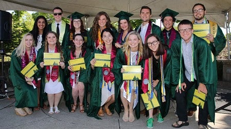 a group of students in graduation regalia, holding diplomas