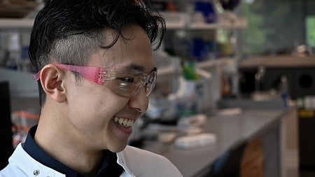 student in lab wearing goggles, smiling off camera