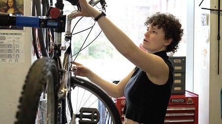 a woman standing in front of a bike on a repair stand, with her hands on the bike