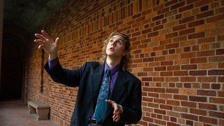 dylan podrabsky wearing a suit and gesturing in front of a brick wall