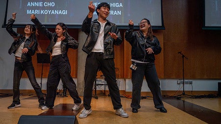 four students dancing onstage in black leather jackets