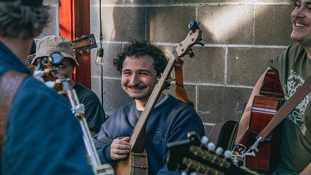 musician holding banjo and smiling at others playing with him