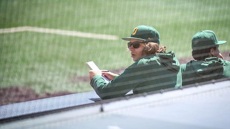 oregon baseball team member watching field from pressbox, notebook in hand