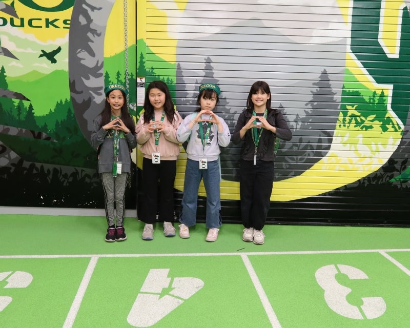four kids in front of Ducks mural making O shape with their hands