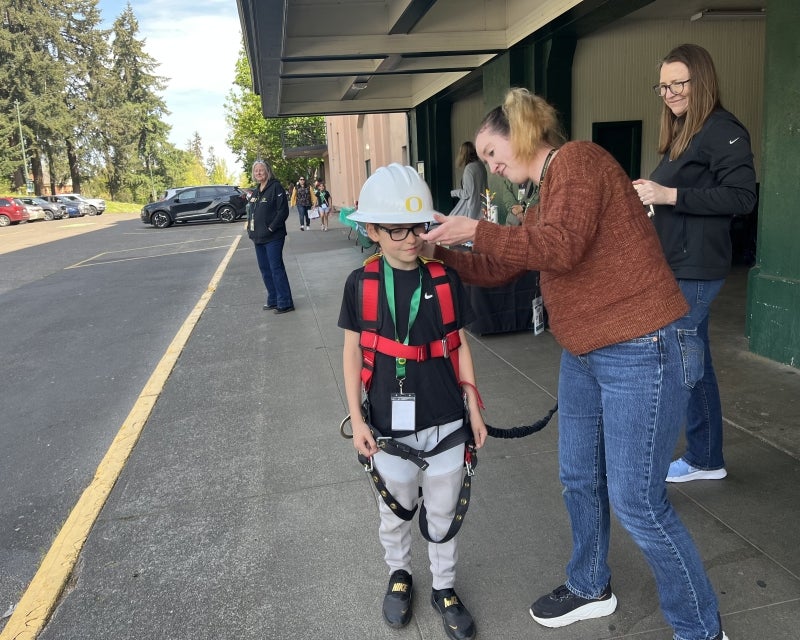 adult helping kid try on a safety hard hat and harnesses