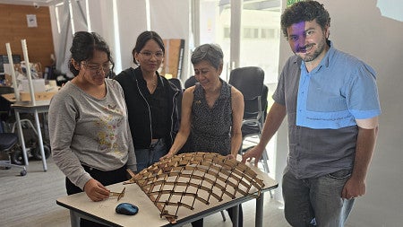 Four people standing looking at a wood structure on a table